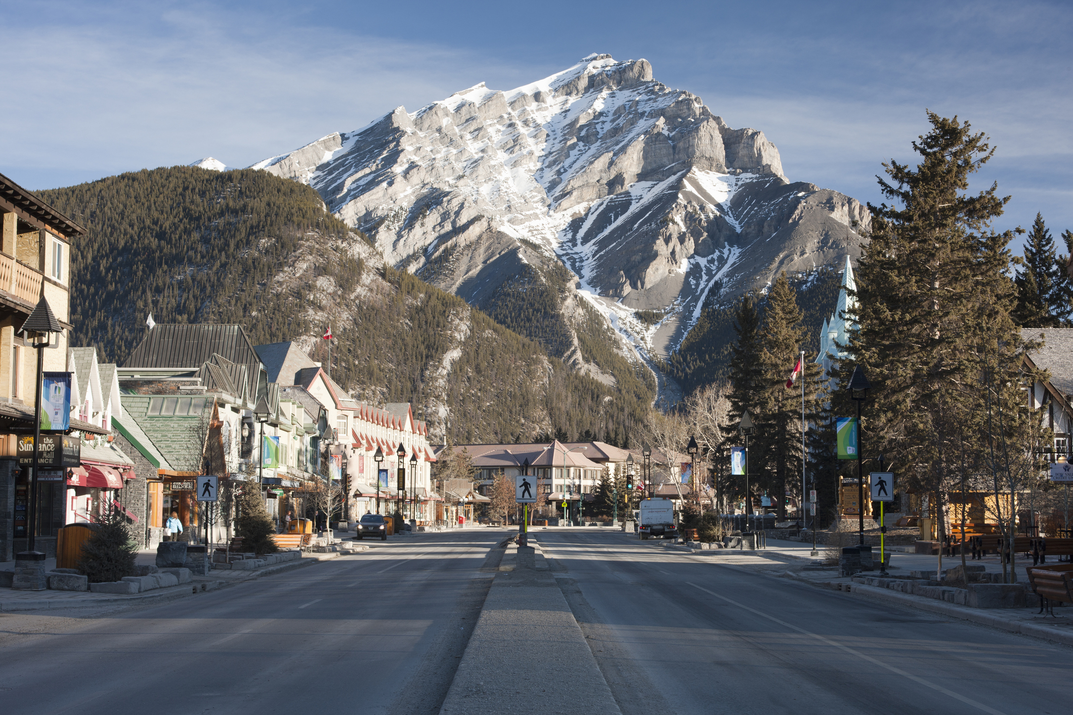 View of a quiet, empty main street in Banff, Canada, with shops on both sides and a snow-covered mountain in the background