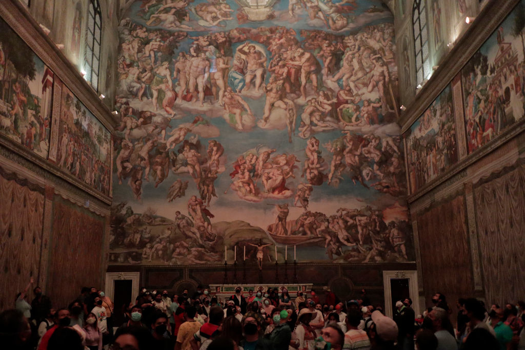 A large group of people touring the Sistine Chapel, featuring Michelangelo&#x27;s famous frescoes on the ceiling and walls