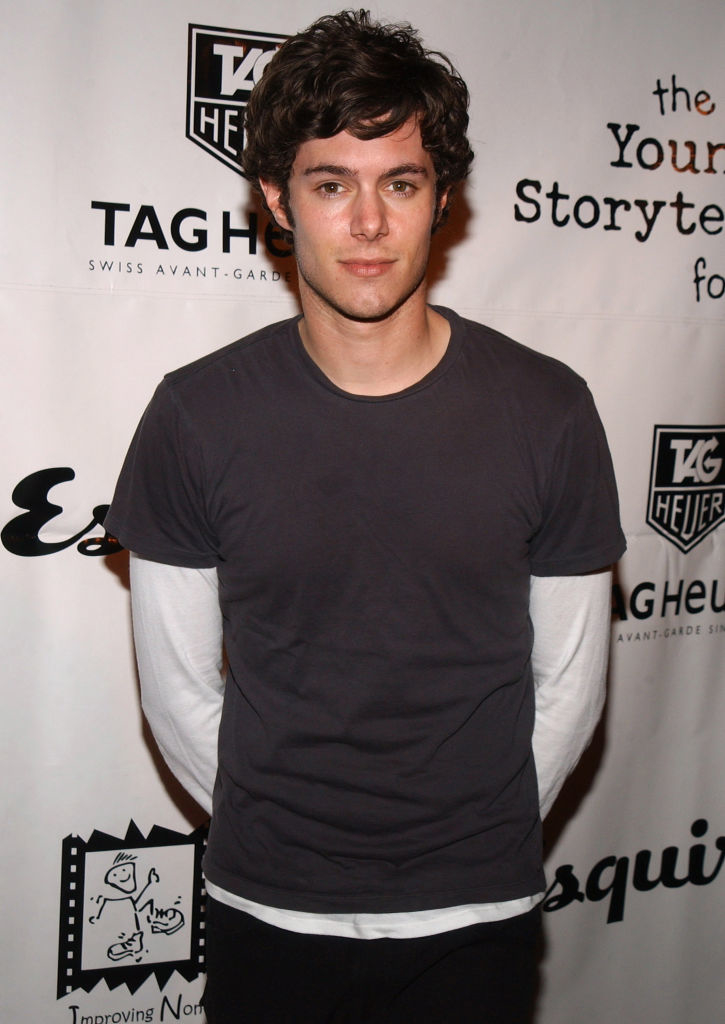 Adam Brody at an event, wearing a dark t-shirt over a long-sleeved shirt, hands behind his back