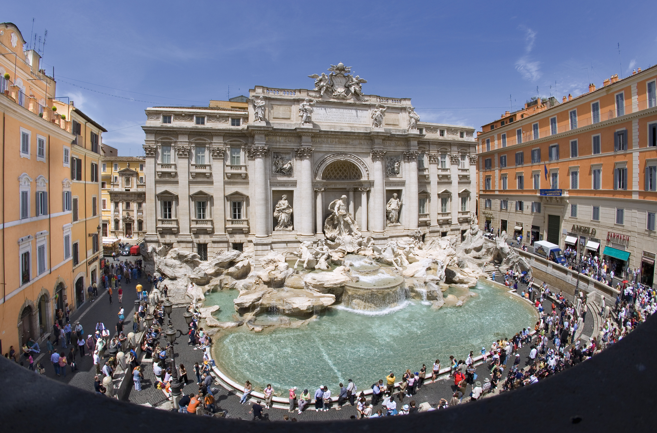 Wide view of the Trevi Fountain in Rome with a crowd of tourists surrounding it and historic buildings in the background