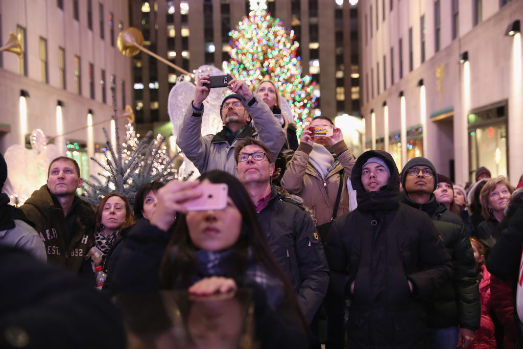 People gather at Rockefeller Center to watch the Christmas tree lighting, capturing the moment on their phones