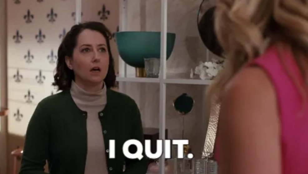 A woman in a green cardigan and beige turtleneck says &quot;I QUIT&quot; while talking to another woman in a pink outfit