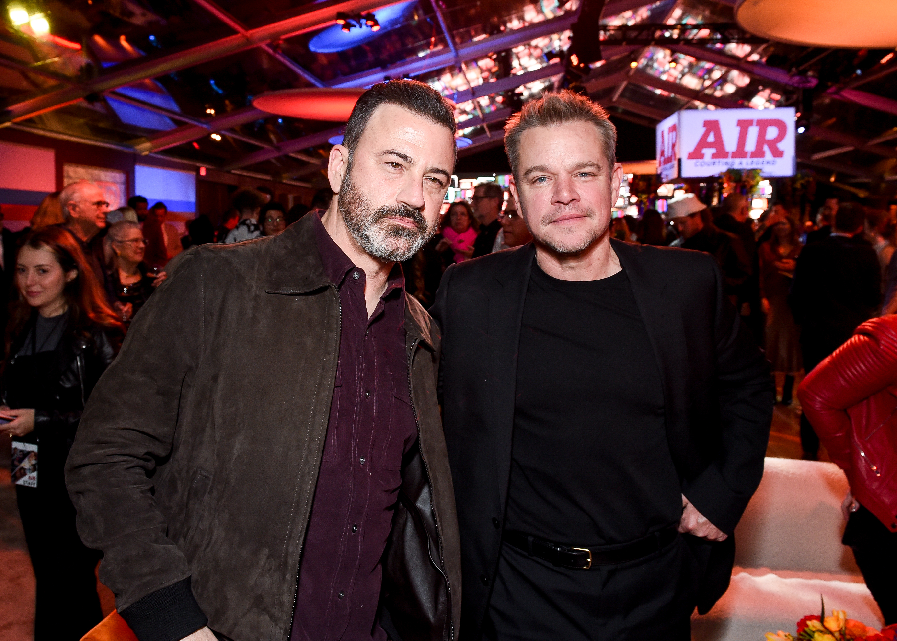 Jimmy Kimmel and Matt Damon at an event, standing closely and smiling. Kimmel wears a dark jacket over a shirt, while Damon wears a black jacket over a black shirt