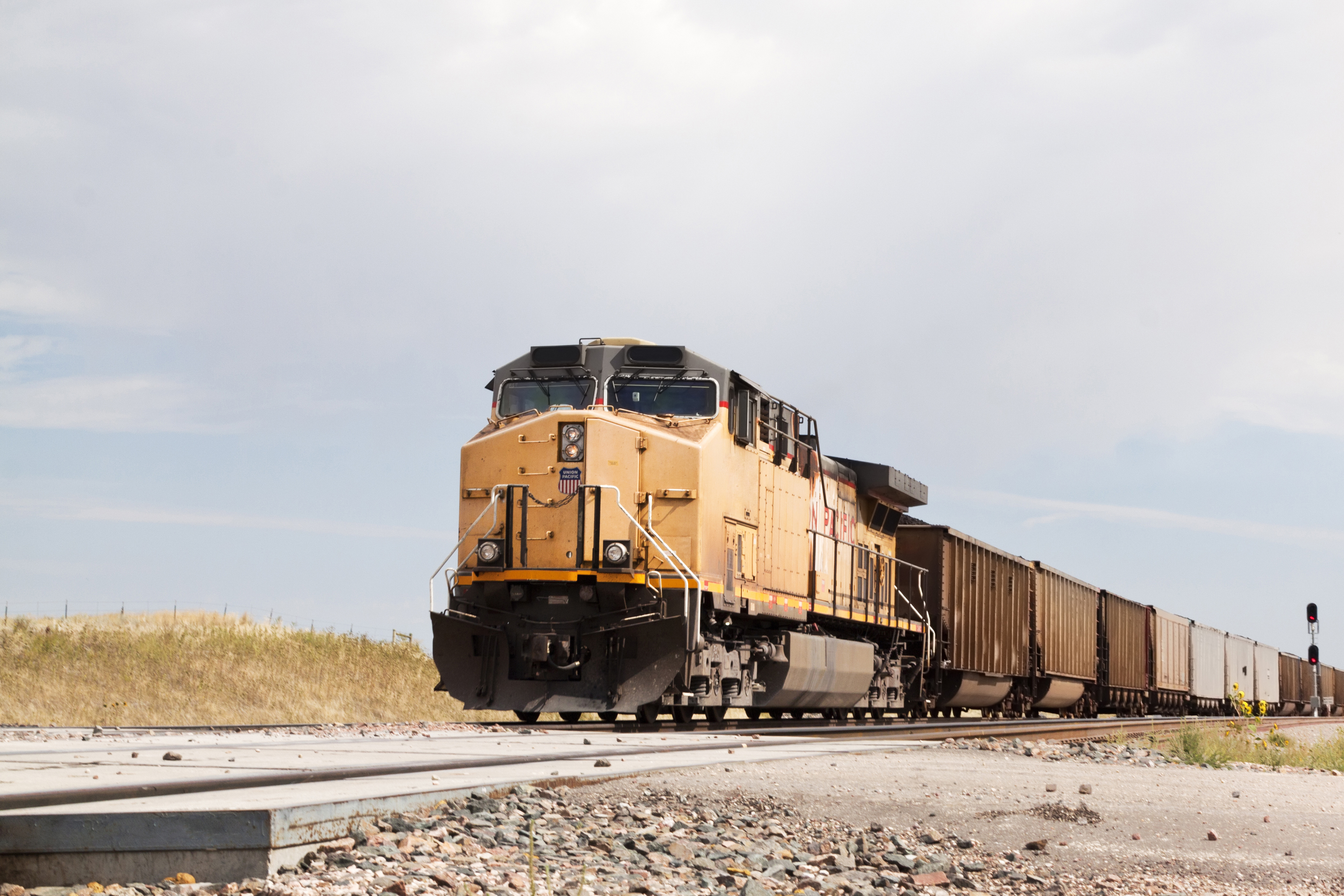 A freight train moving on tracks in an open landscape under a cloudy sky