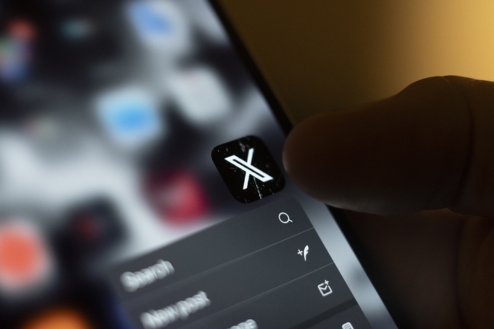 Close-up of a hand holding a smartphone, focusing on the X app icon on the screen