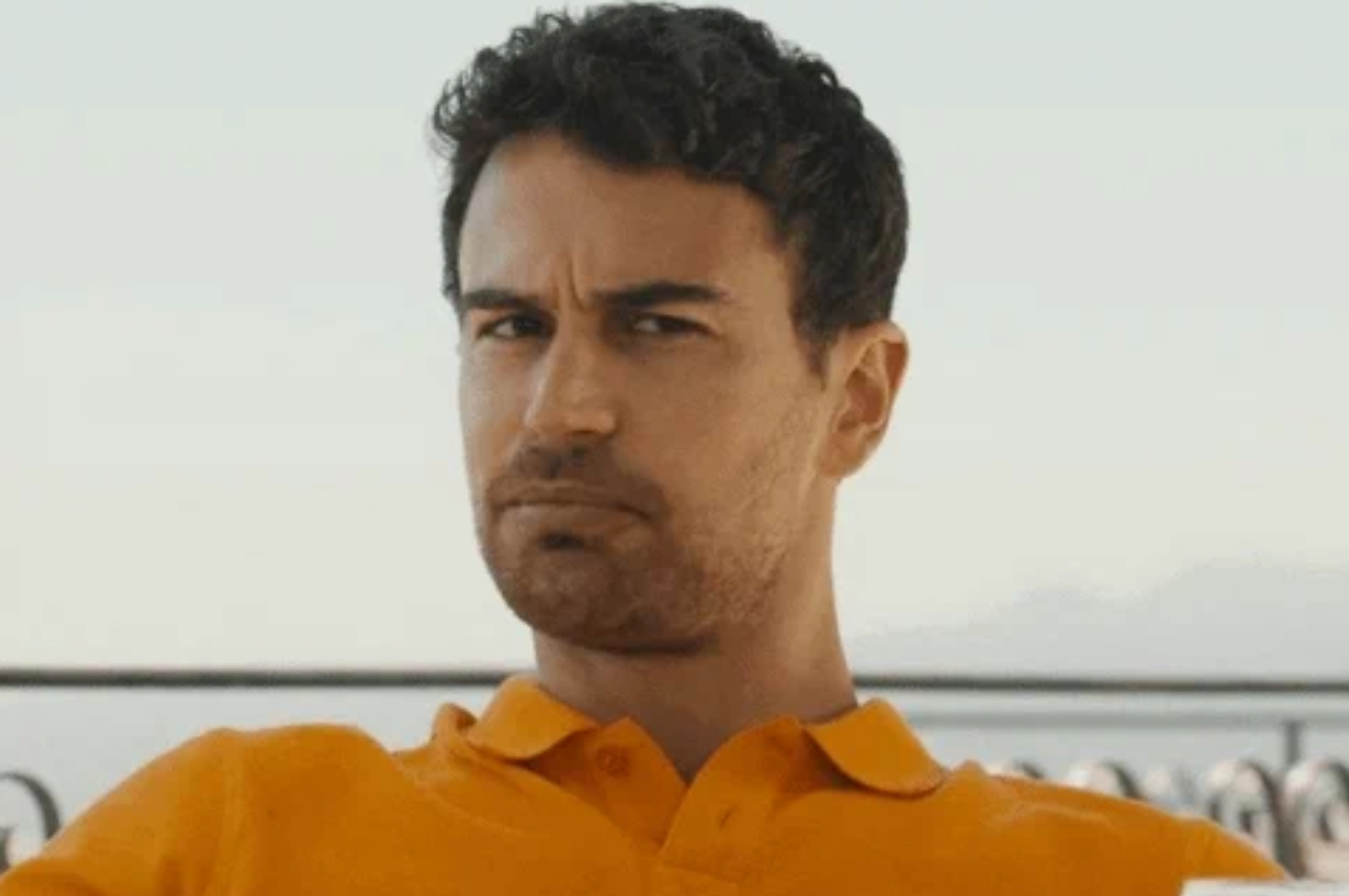 A man frowning and looking slightly to the side, dressed in a casual short-sleeve shirt, with an outdoor setting in the background