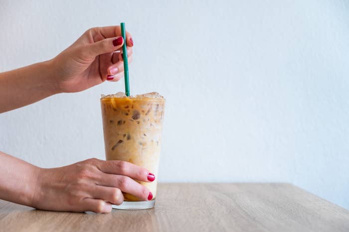 Hands stirring an iced coffee with a straw on a wooden table