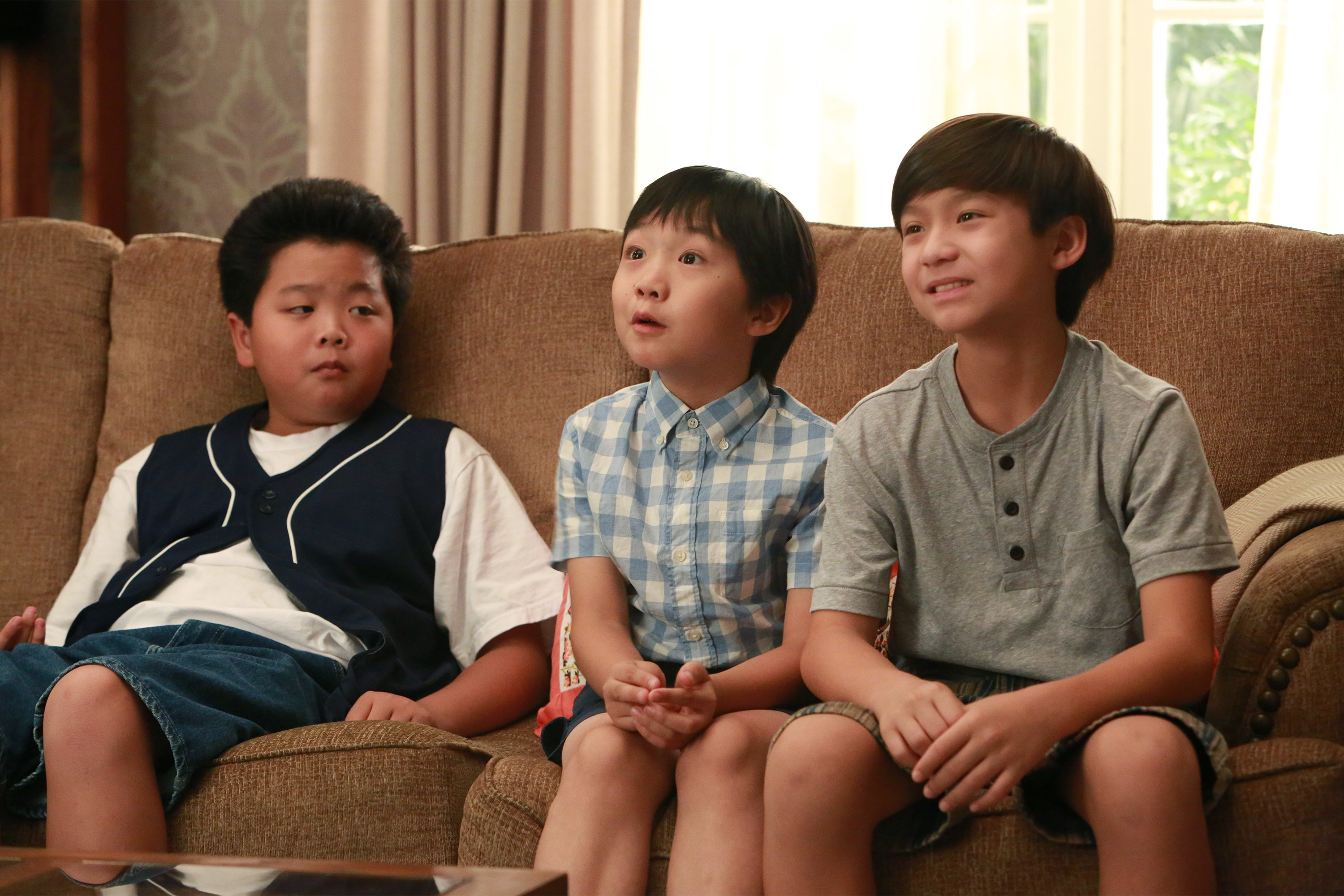 Three children, Hudson Yang, Ian Chen, and Forrest Wheeler, sit together on a couch, chatting and smiling. Their attire is casual