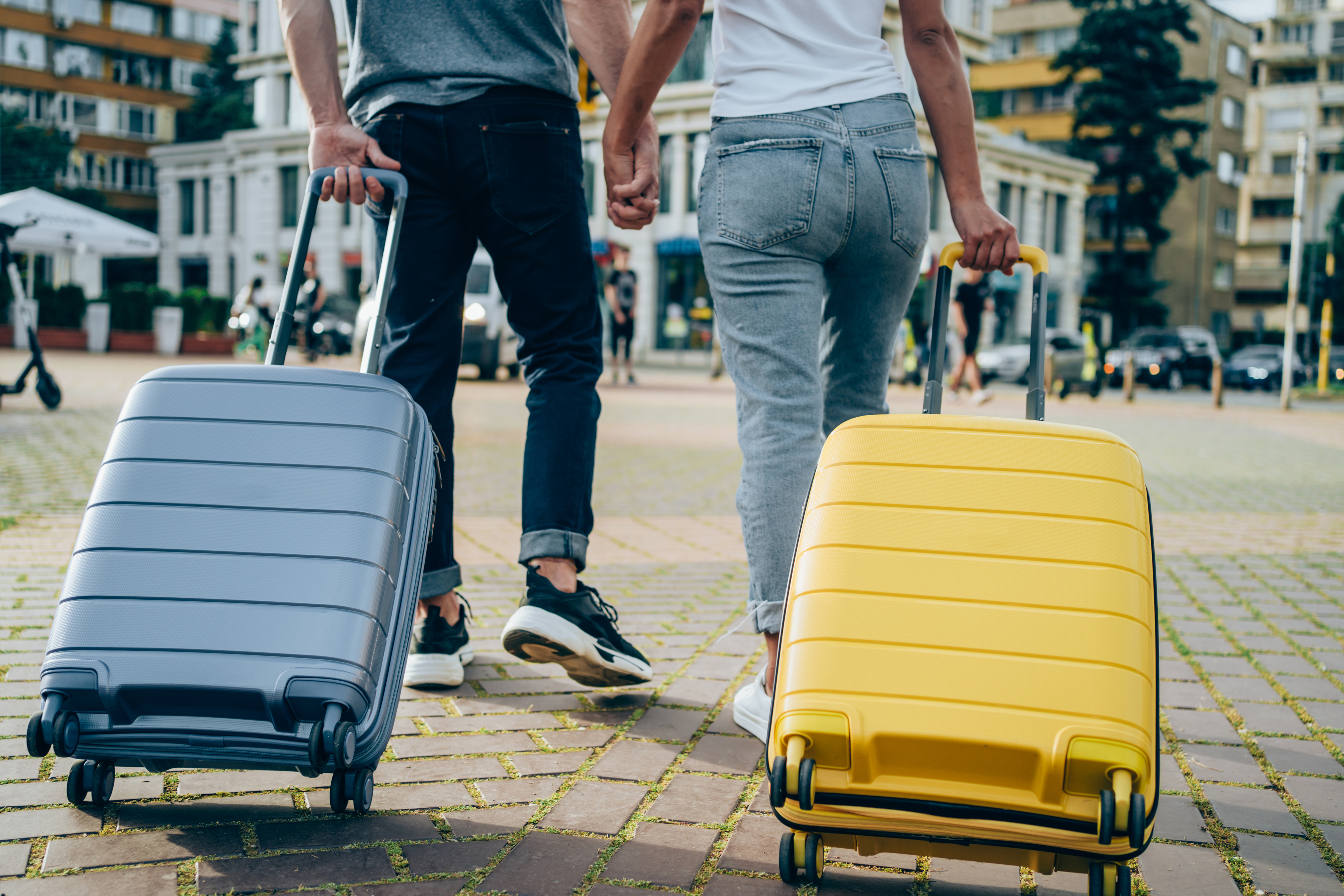 Two people holding hands and walking with rolling suitcases in an urban area