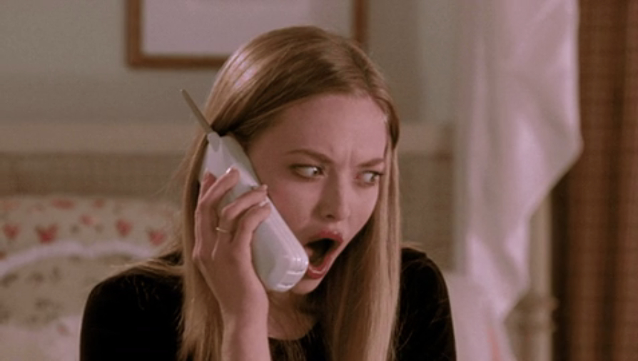 Amanda Seyfried, in a shocked expression, holding a cordless phone to her ear. Her eyes are wide open with her mouth agape