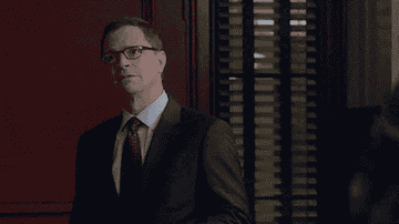David Rosen, in a suit and tie, wearing glasses, stands in a room and talks.