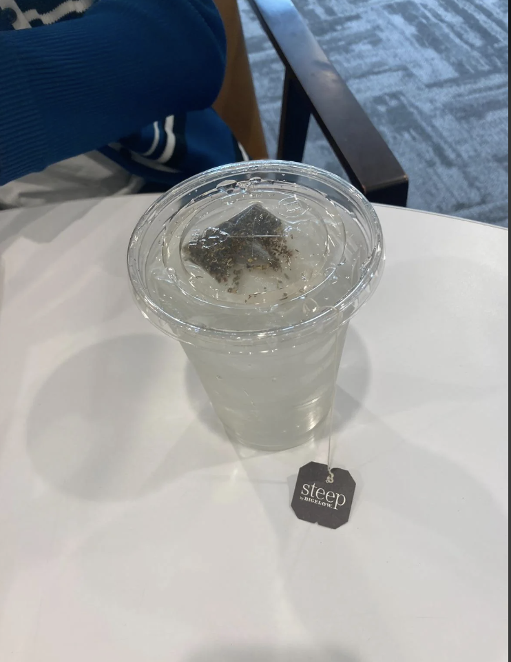 A clear plastic cup filled with iced water and a tea bag labeled "steep" on a table