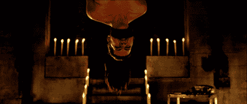 Lorna in Hostel 2 hangs upside down with a gag over their mouth in a dimly lit room with candles.
