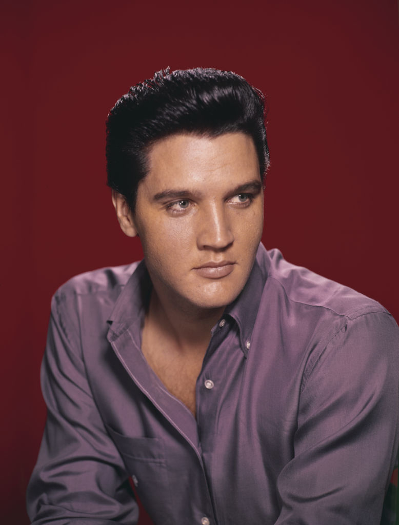 Elvis Presley poses against a plain backdrop in a collared shirt