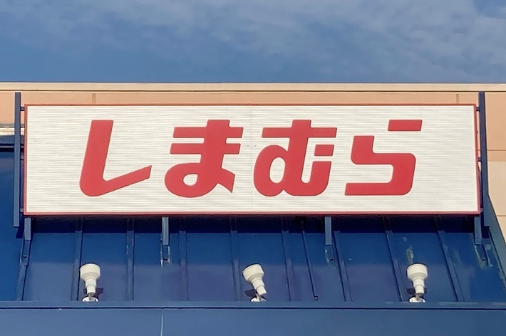 The image shows a storefront with a sign displaying Japanese text. The text reads &ldquo;しまむら.&quot;