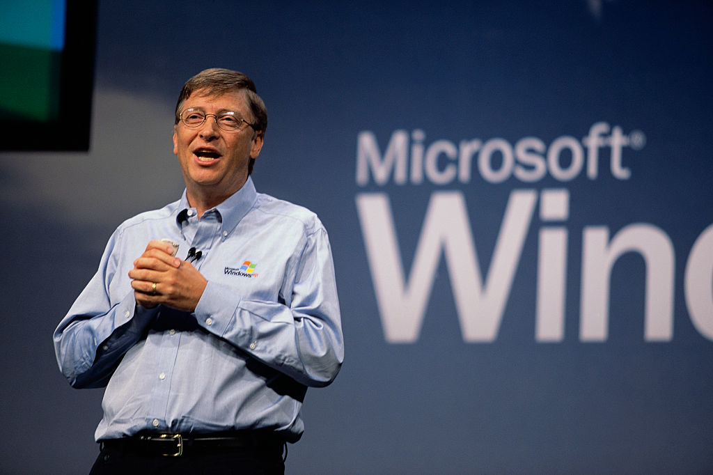 Bill Gates, wearing a Microsoft shirt, speaks on stage at a Microsoft Windows event