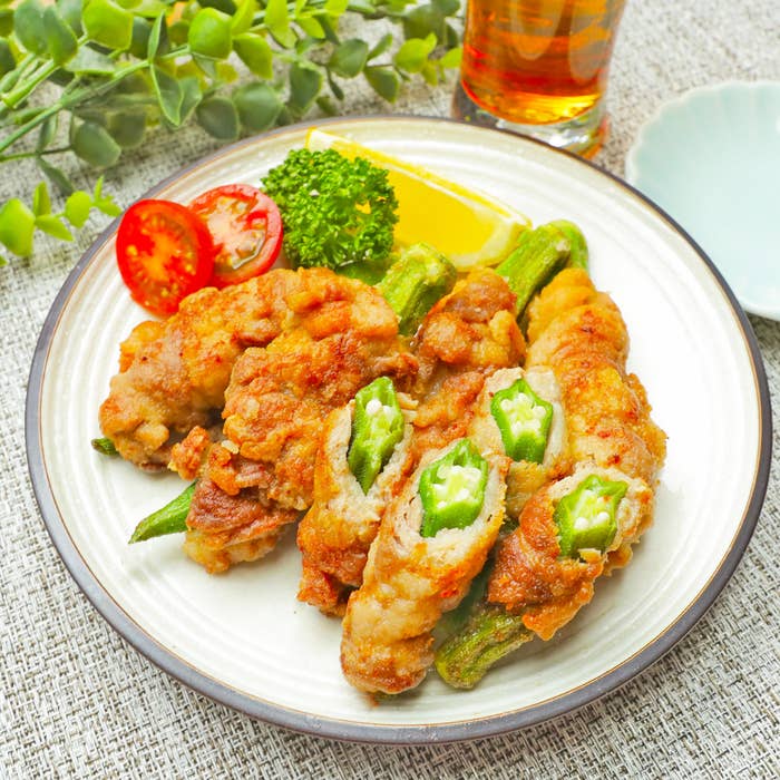 皿に盛られた揚げ物料理。オクラが巻かれている一部の揚げ物が切られ、中身が見えている。トマト、レモン、パセリも添えられている。