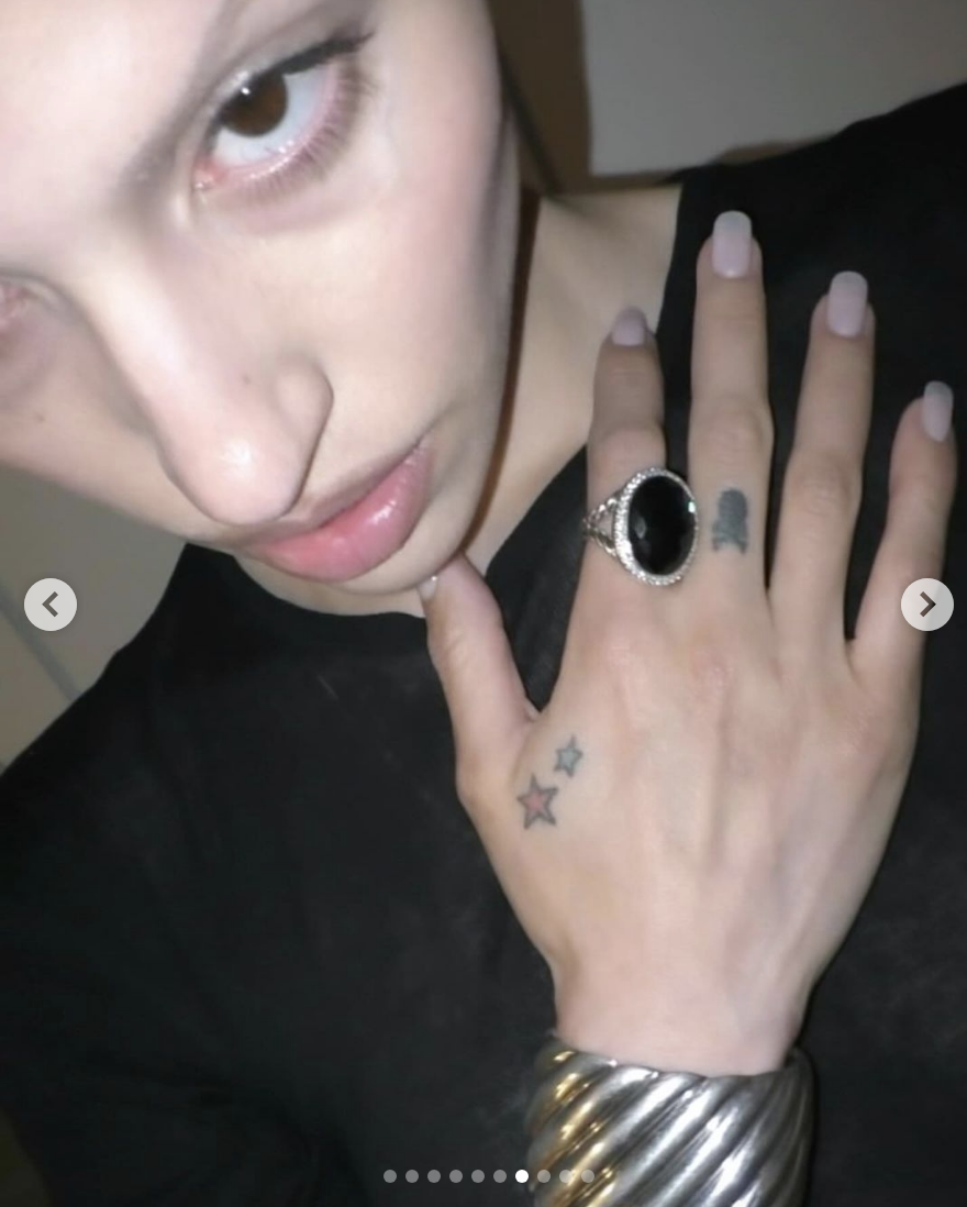 Gabbriette shows off a hand adorned with a large black ring, two small star tattoos, and a band of metallic bangle bracelets