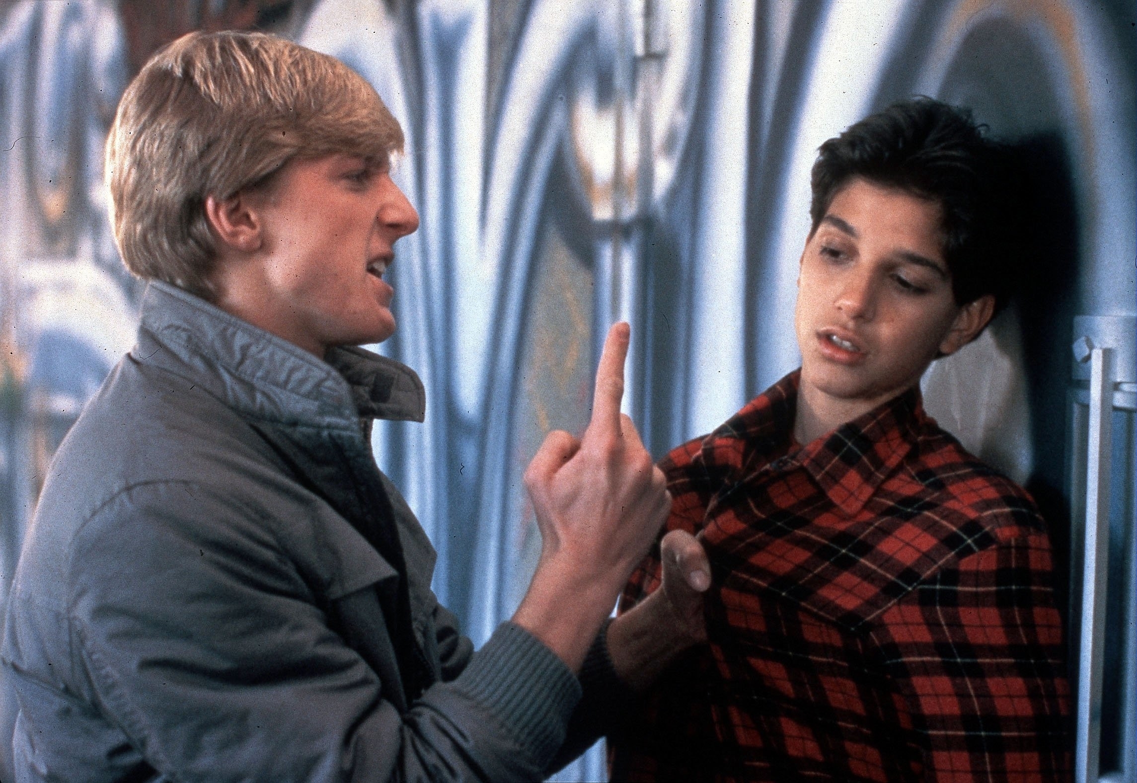 William Zabka points at Ralph Macchio, pinned against a wall, in a dramatic scene from "The Karate Kid."