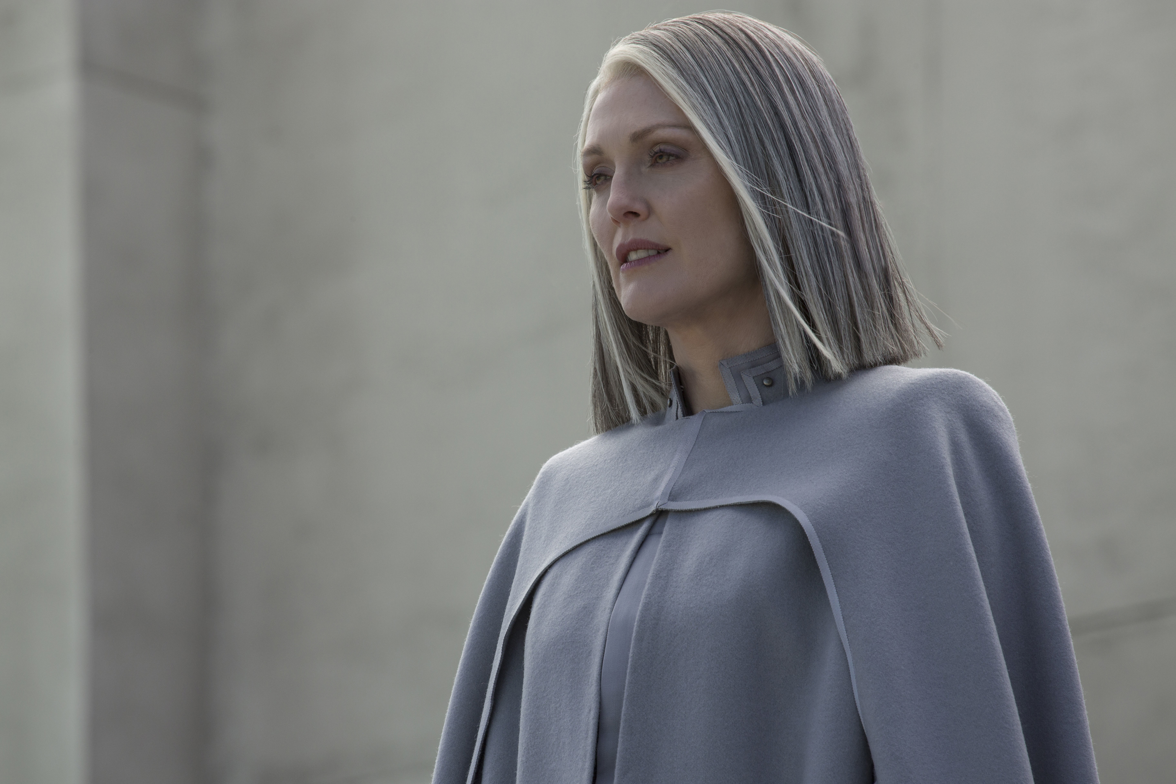 Julianne Moore as President Alma Coin stands in a gray cape with a high collar in a still from the movie