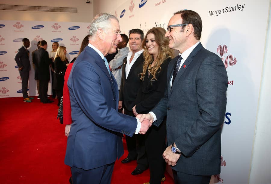 Prince Charles and Kevin Spacey shaking hands on a red carpet, with several other people in the background