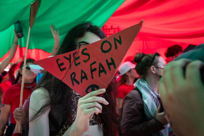 People at a protest holding a red triangular sign reading &quot;Eyes on Rafah.&quot;
