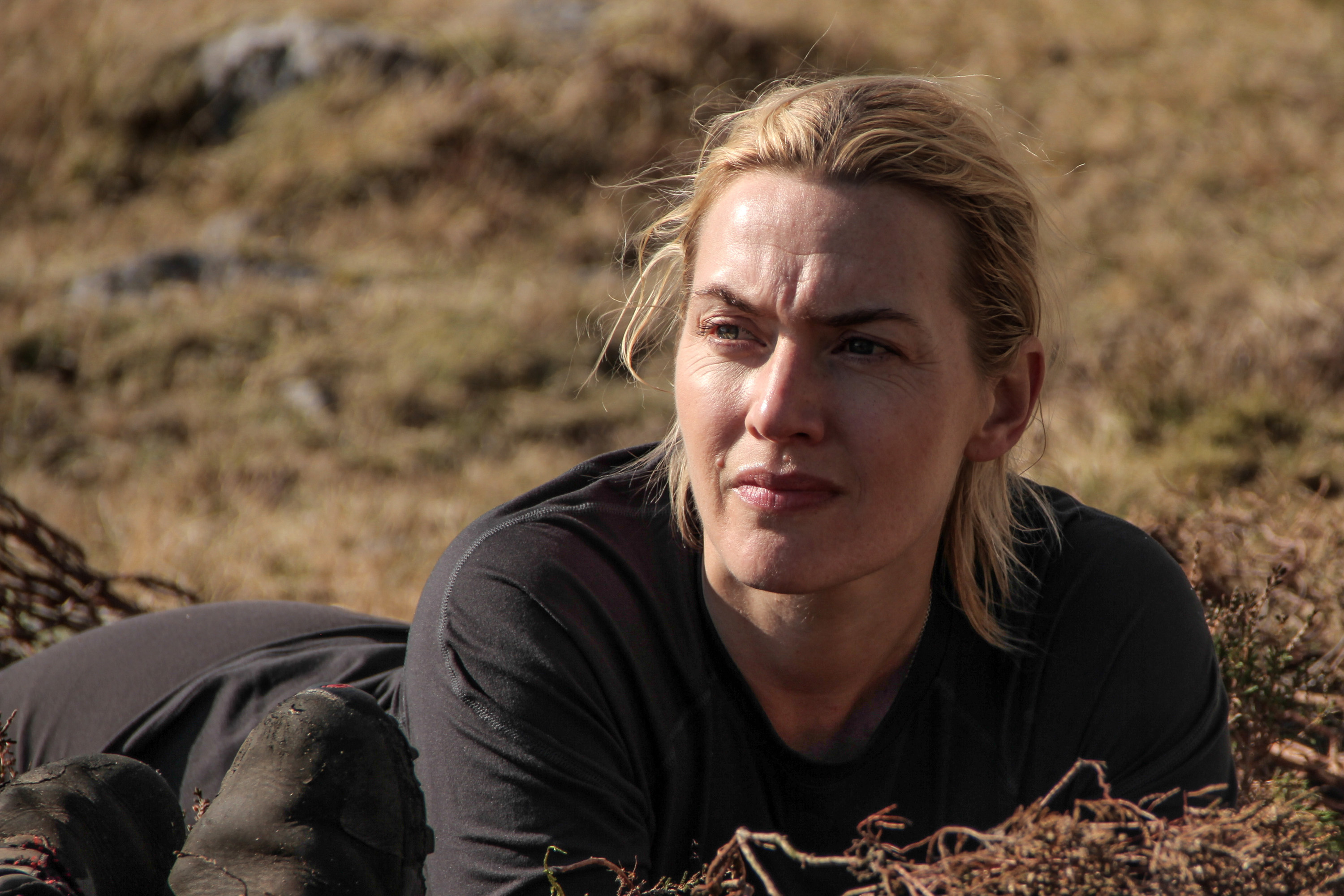 Kate Winslet lying on the ground outdoors, dressed in casual attire