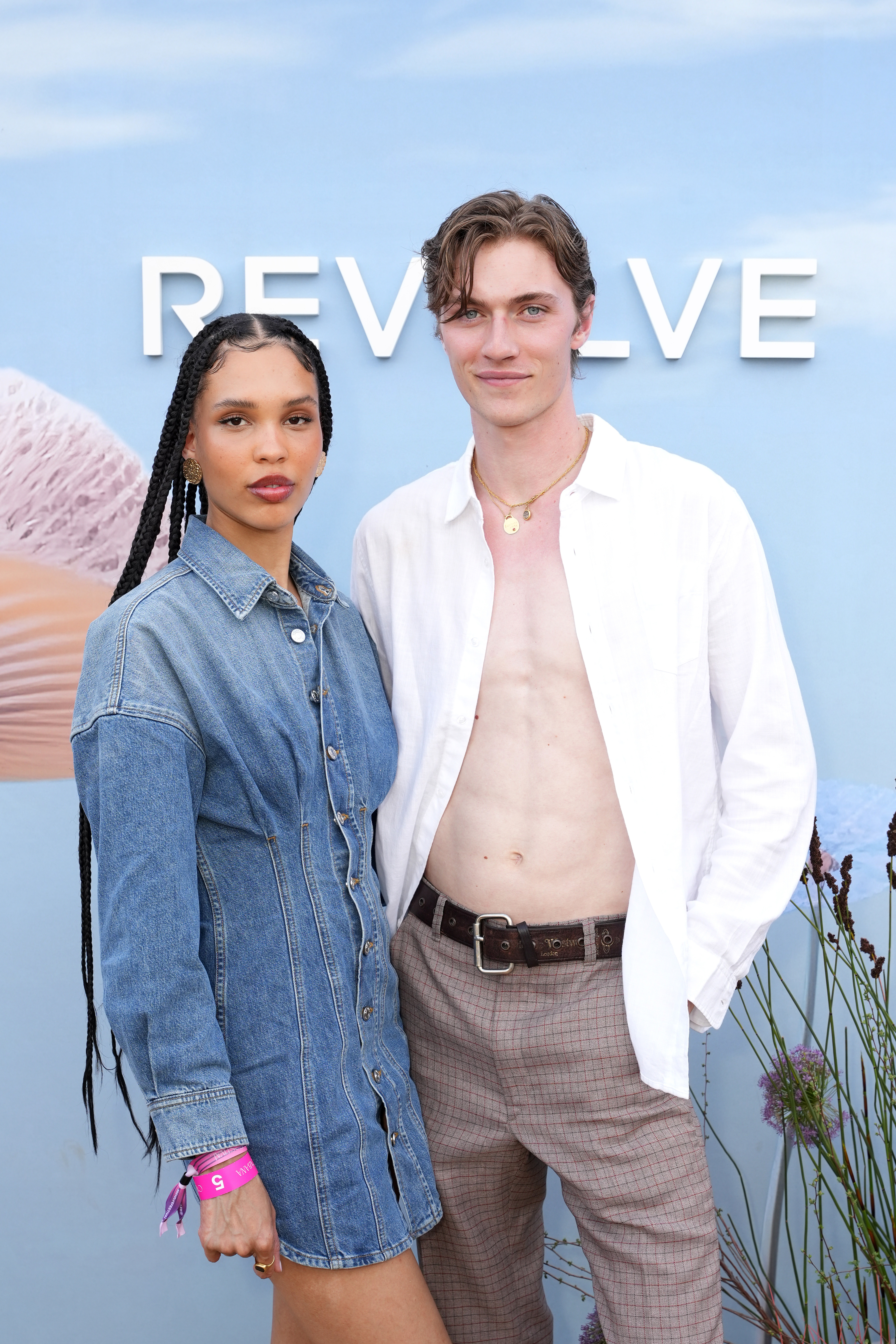 April Alexander in a denim dress and Christian Hogue in an unbuttoned white shirt and brown pants at the Revolve event