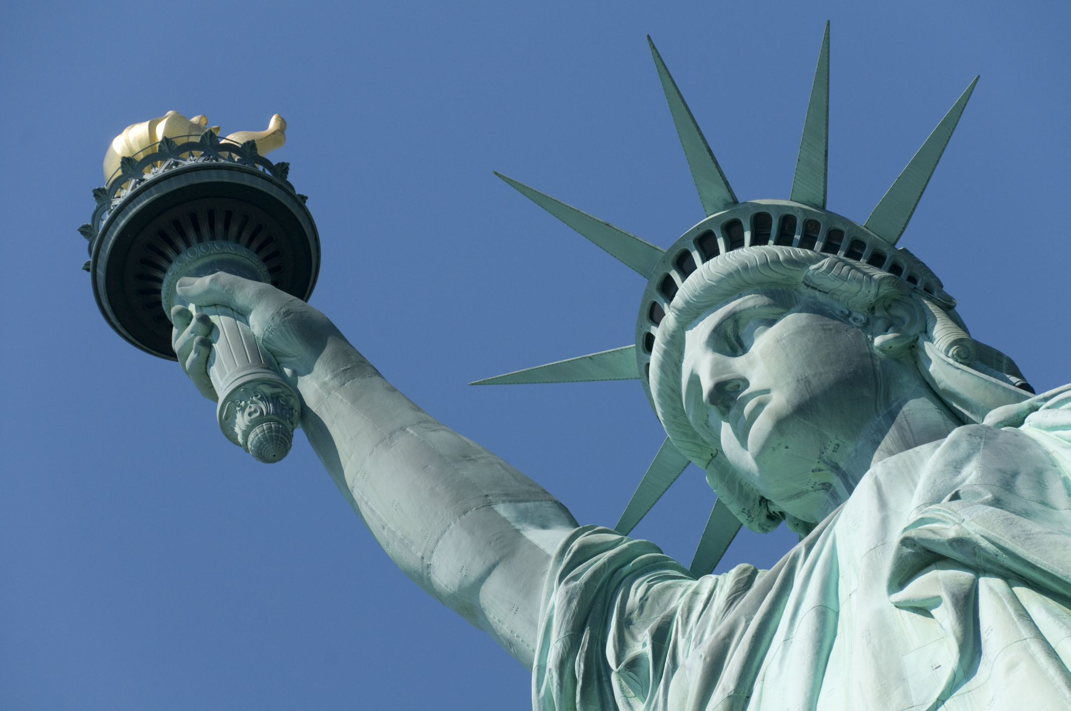 Statue of Liberty, viewed from below, holding the torch aloft against a clear sky