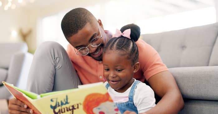 An adult man and a young girl read a book titled "Just Ginger" together on a couch, both smiling and engaged in the story