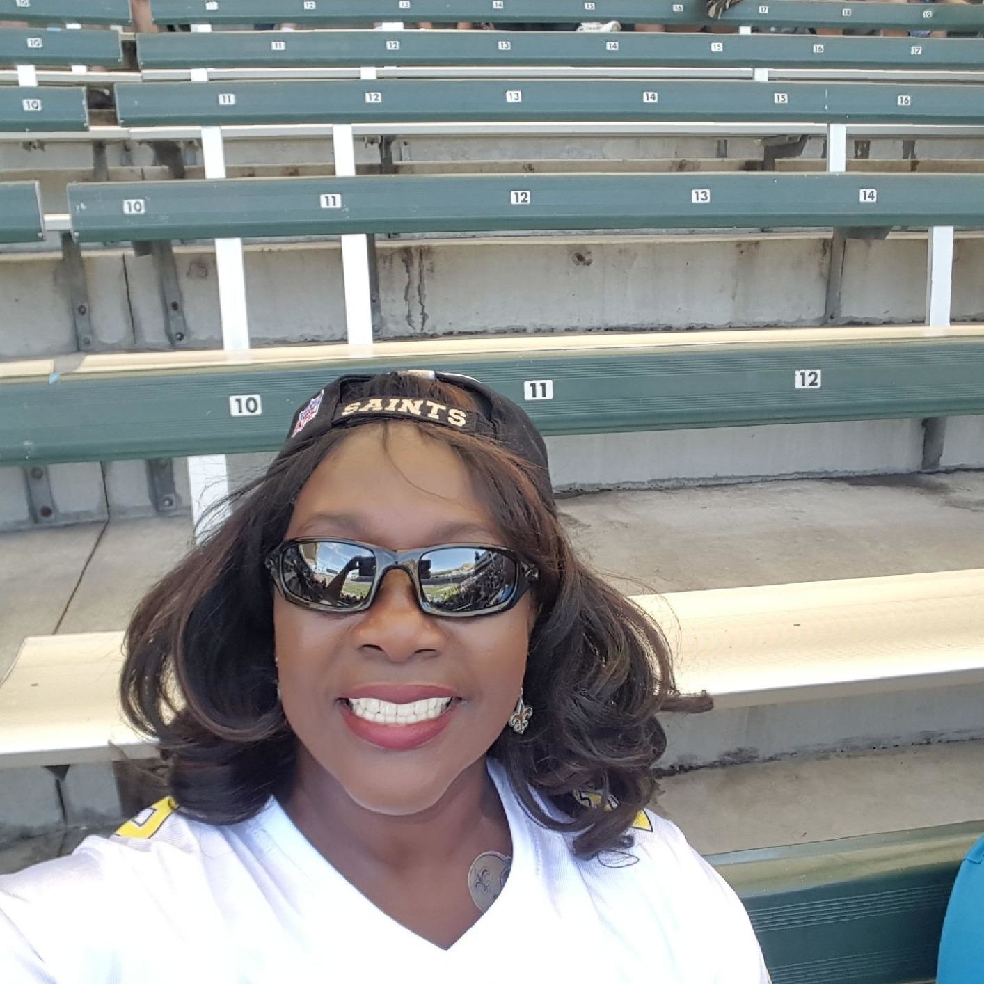 Woman in a &quot;Saints&quot; cap and sunglasses smiles in selfie at a mostly empty stadium