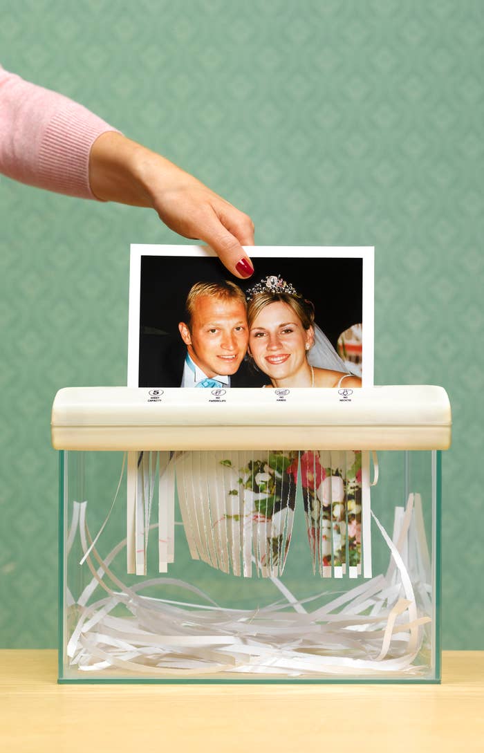 A hand shreds a wedding photo of a smiling couple in formal attire