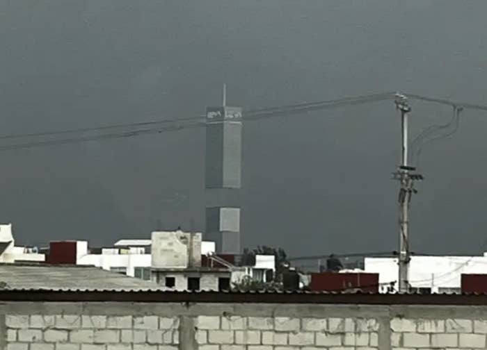 Tall building under construction in a city, with scaffolding visible. Foreground includes rooftops and utility poles