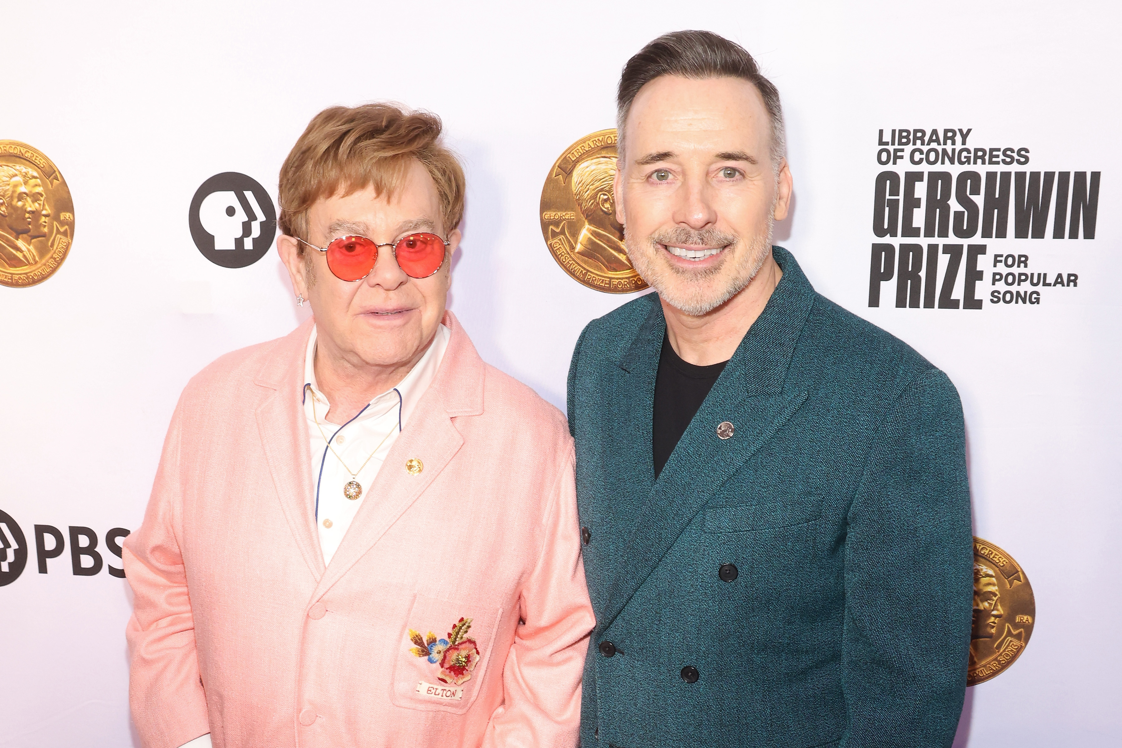 Elton John, in a pink suit, and David Furnish, in a teal suit, pose together at the Library of Congress Gershwin Prize for Popular Song event