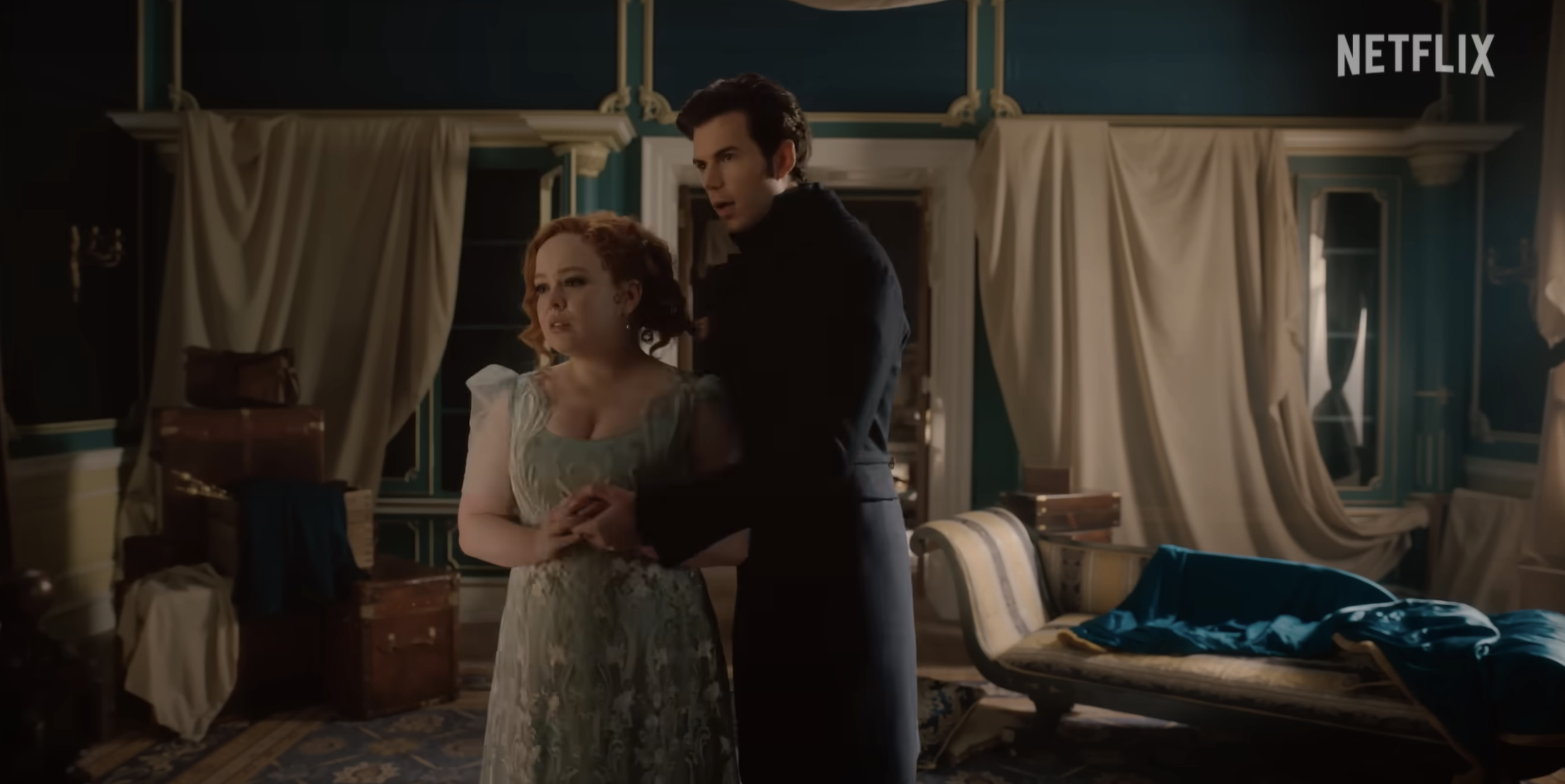 Nicola Coughlan and Luke Newton in period costumes, standing in an elegant room with antique furniture, from the Netflix series &quot;Bridgerton.&quot;