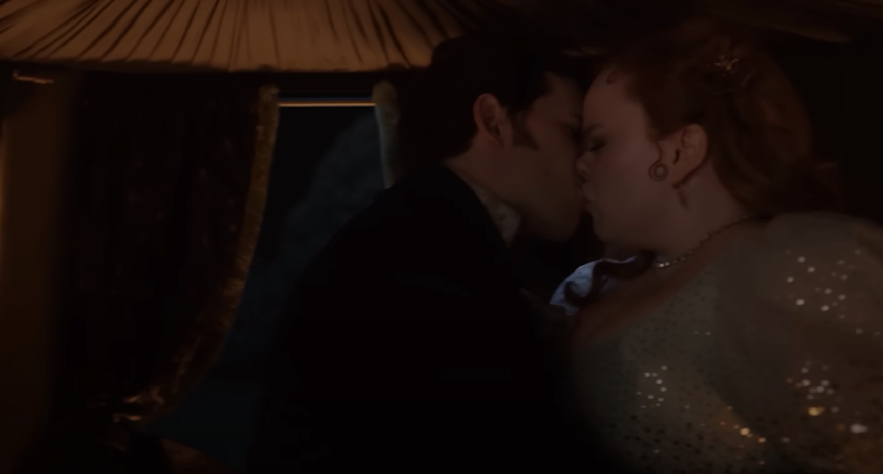 Nicola Coughlan and Luke Newton share a kiss in a dimly lit scene from &quot;Bridgerton.&quot; Nicola's character wears an elegant gown with subtle sparkling details