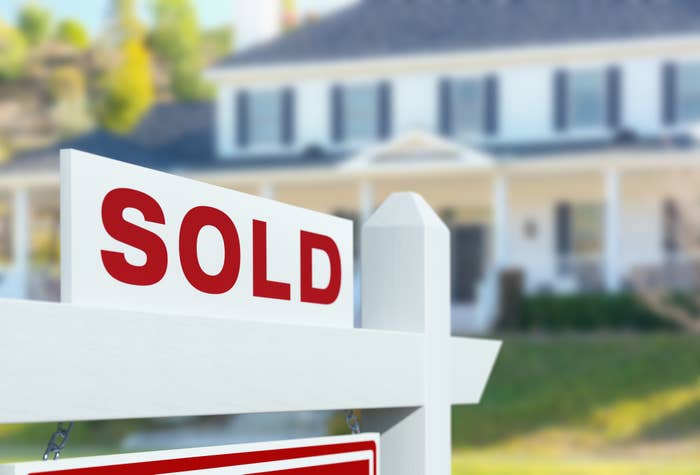 Real estate sign with "SOLD" in front of a suburban house