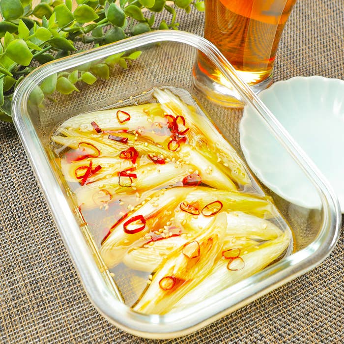 ガラス容器に盛られたネギのマリネ、上にはスライスされた赤唐辛子がトッピングされています。旁に飲み物が見えます。