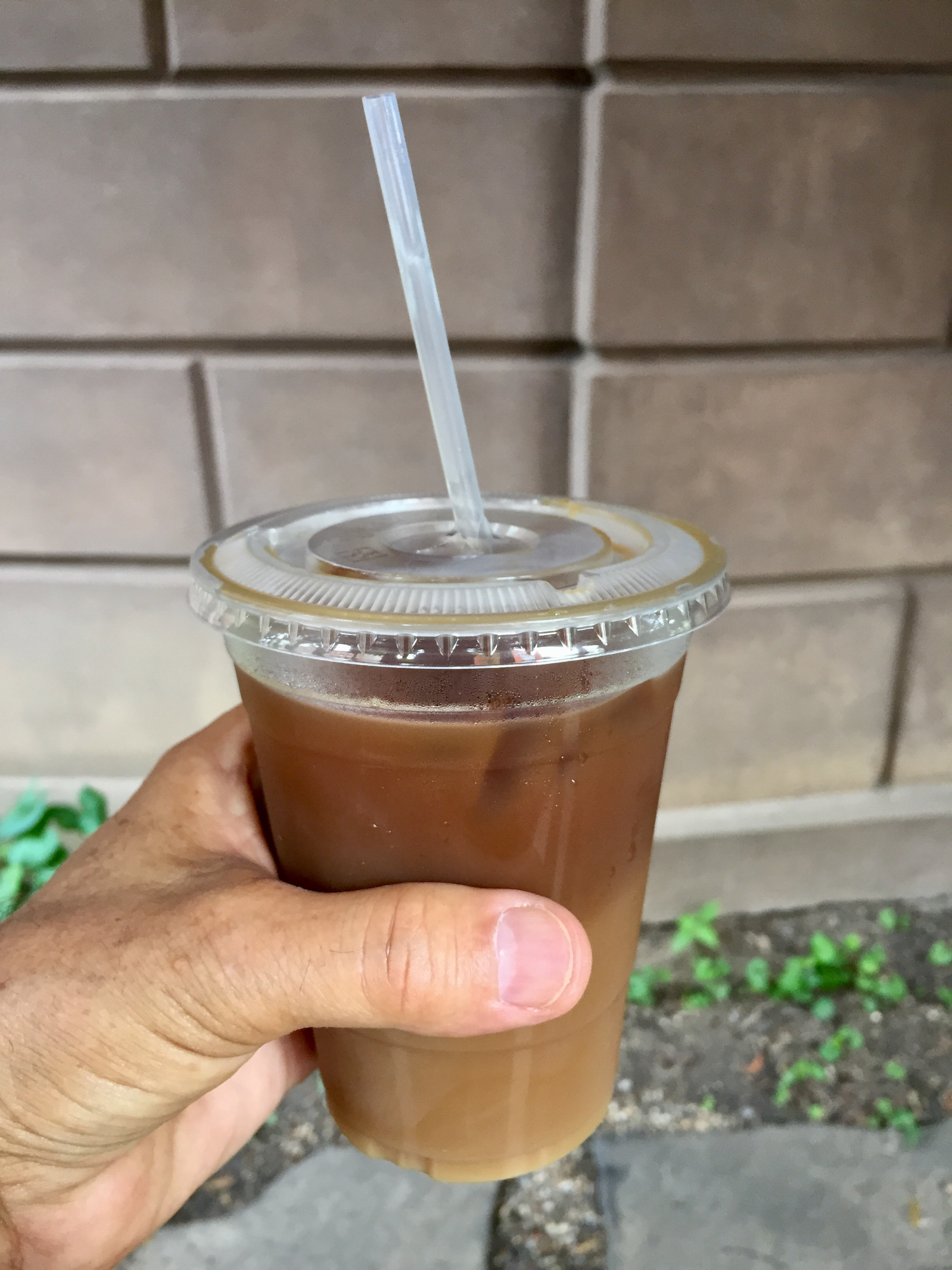A hand holding a plastic cup filled with iced coffee with a straw inserted