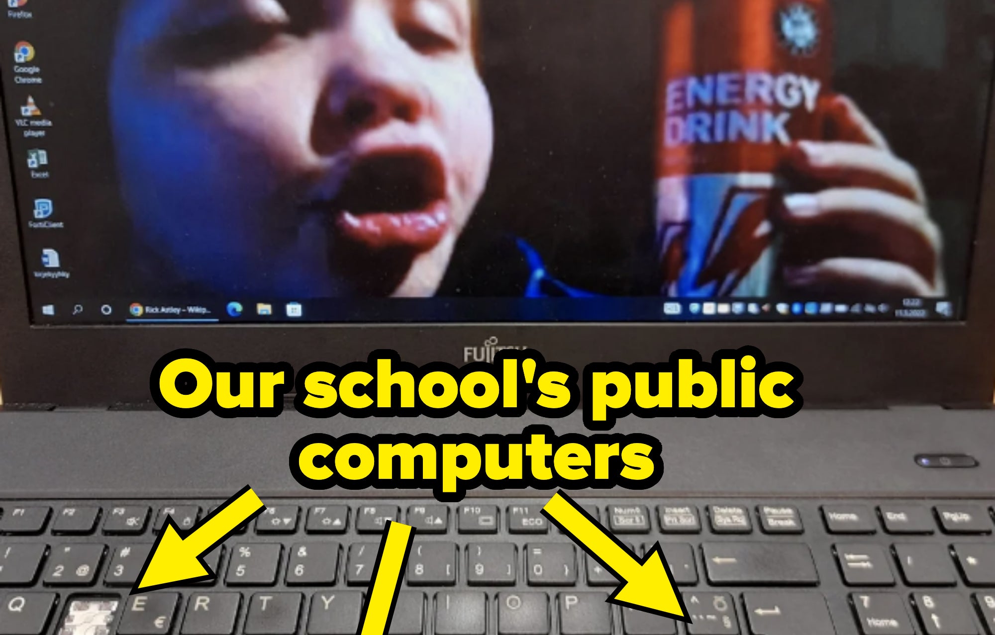 A child is seen on a Fujitsu laptop screen, holding an energy drink can and making a playful face