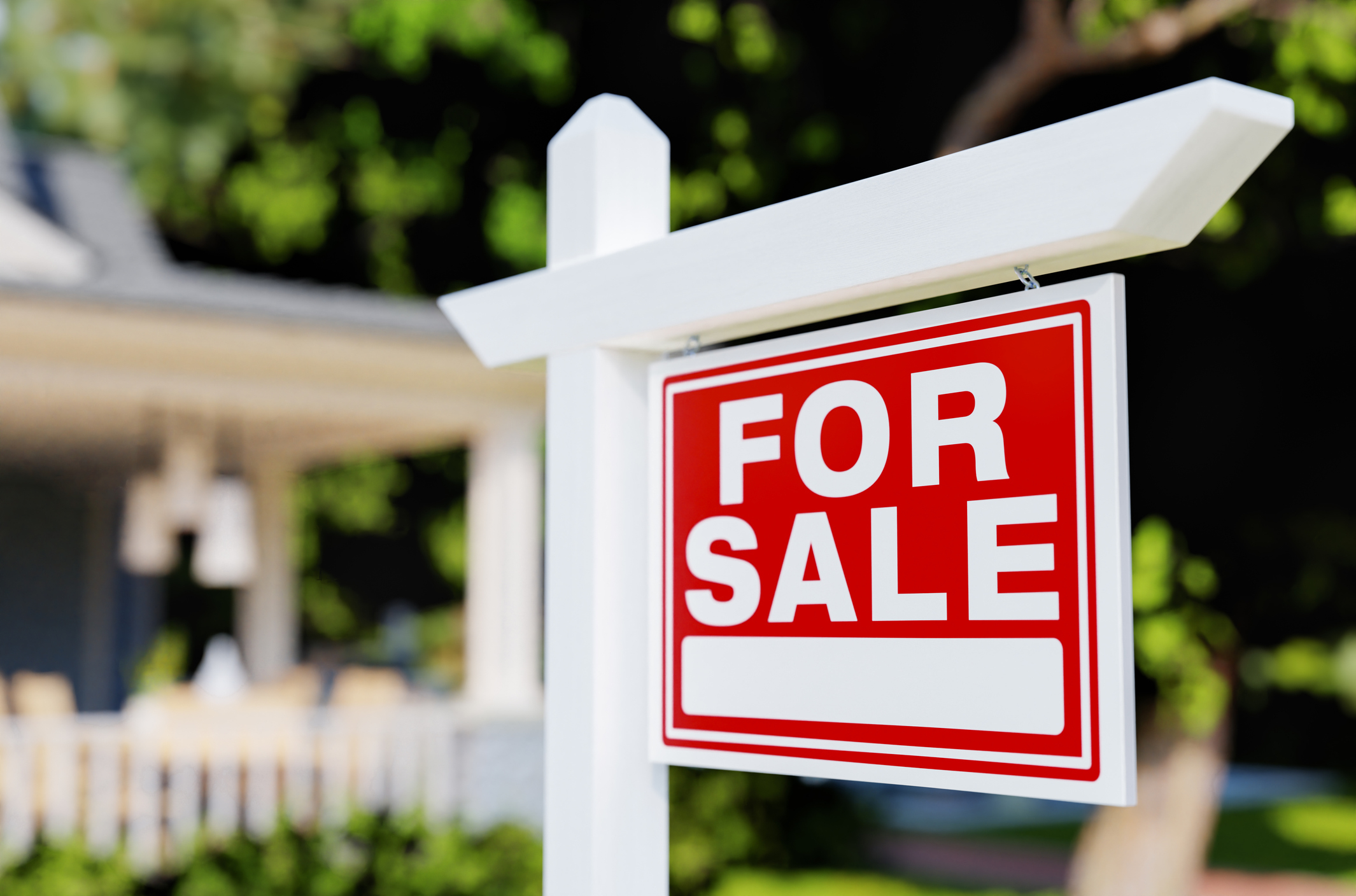 "For Sale" sign in front of a house with a blurred background