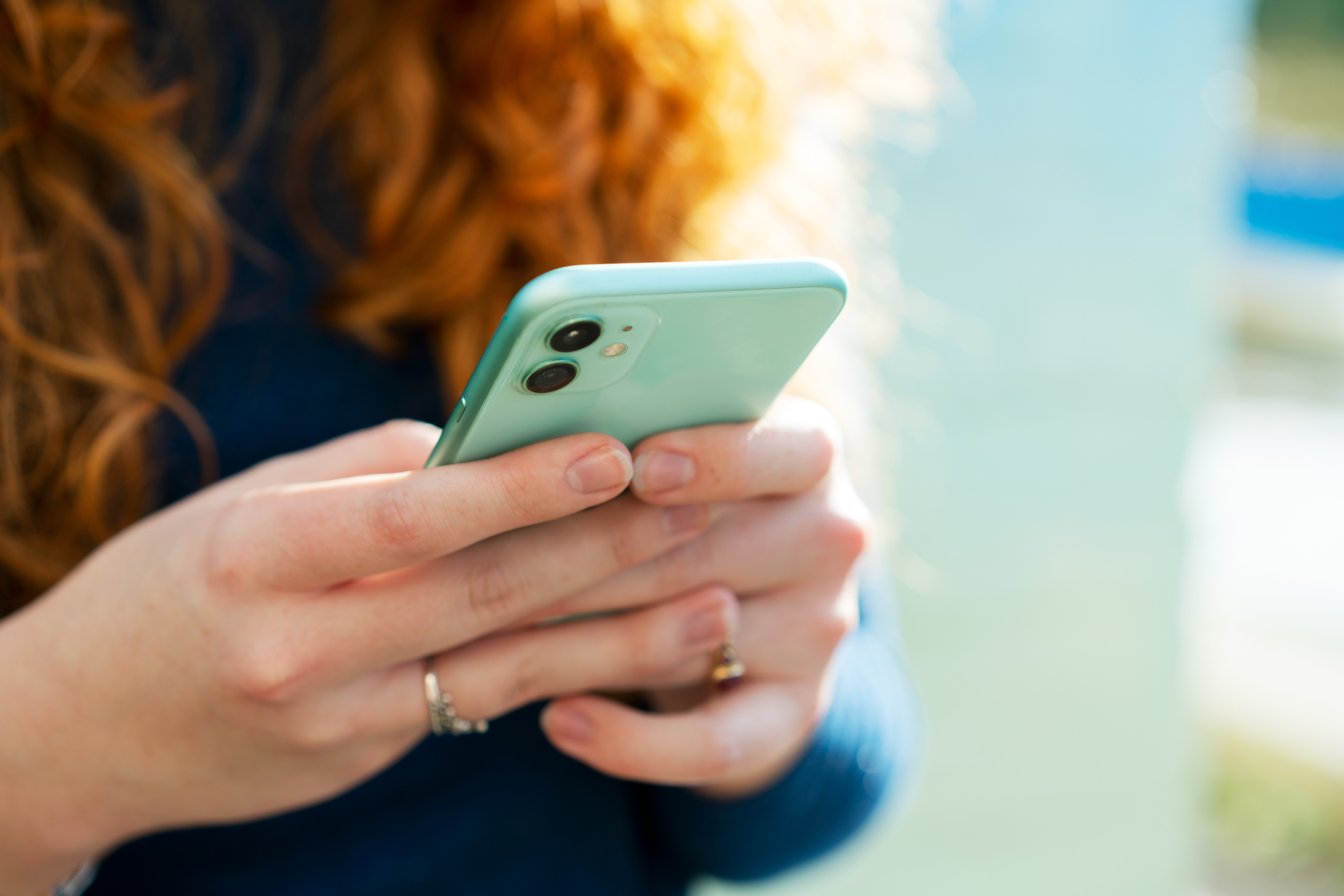 Person with long curly hair holding a smartphone, texting or reading something on the screen
