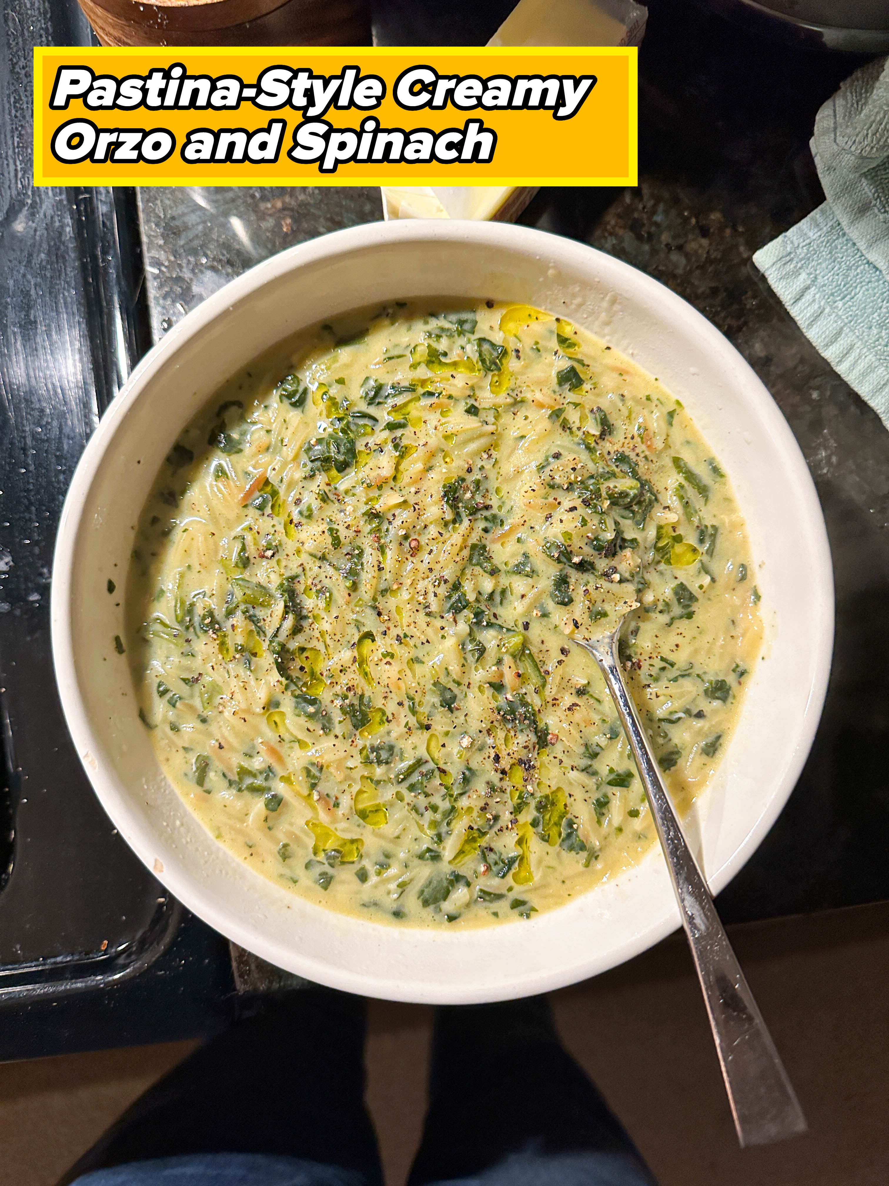 A bowl of creamy spinach soup with a spoon in it, shown from above. There is a bar of butter and some kitchen items in the background