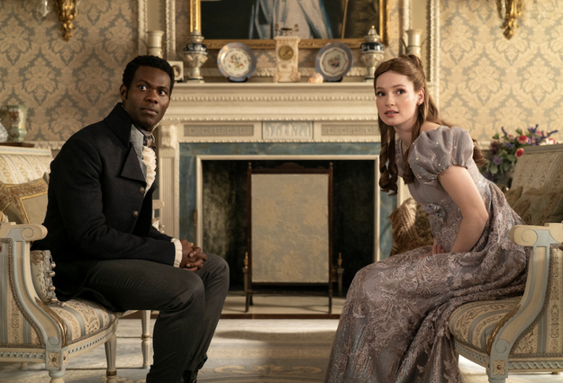 Martins Imhangbe y Phoebe Dynevor en una escena de un drama de época, ambos sentados en una elegante sala de estar con decoración clásica