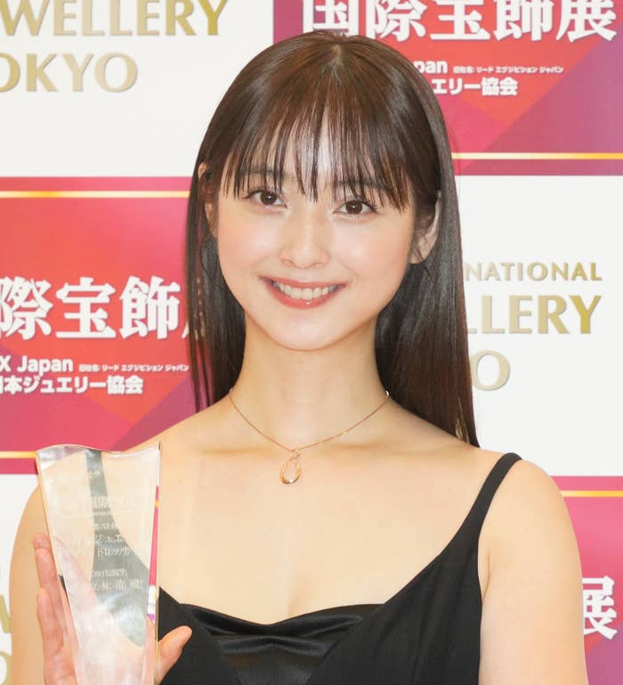 女性が黒いドレスを着てトロフィーを持っている。背景には「国際宝飾展」「TOKYO International Jewellery」が書かれている文字パネル。