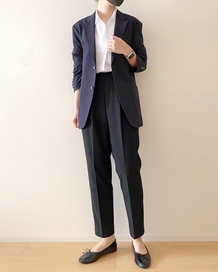 人物が白いシャツに黒いジャケットとズボンを着用し、黒い靴を履いています。