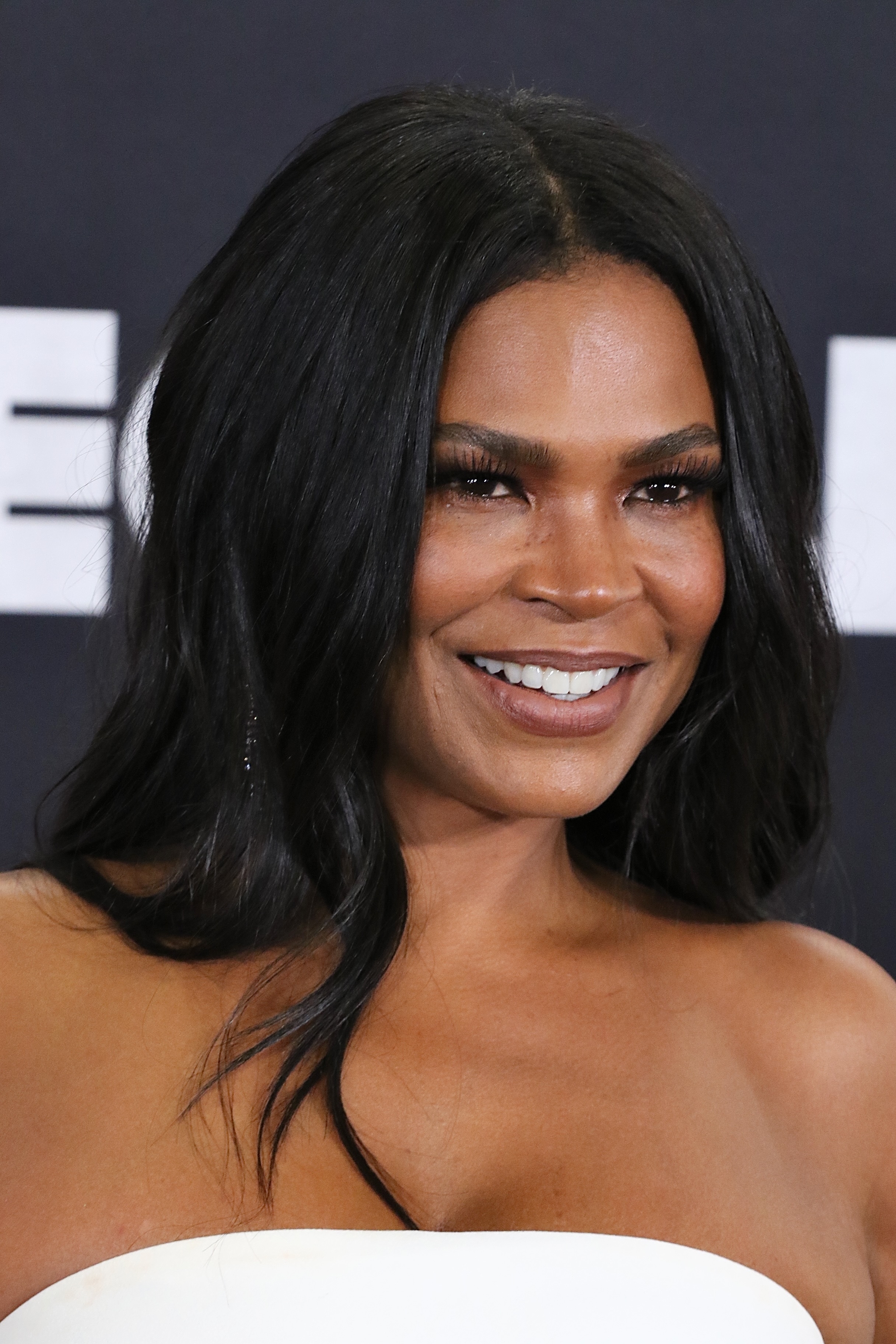 Nia Long smiles at a red carpet event, wearing an elegant strapless dress and long hair styled in soft waves