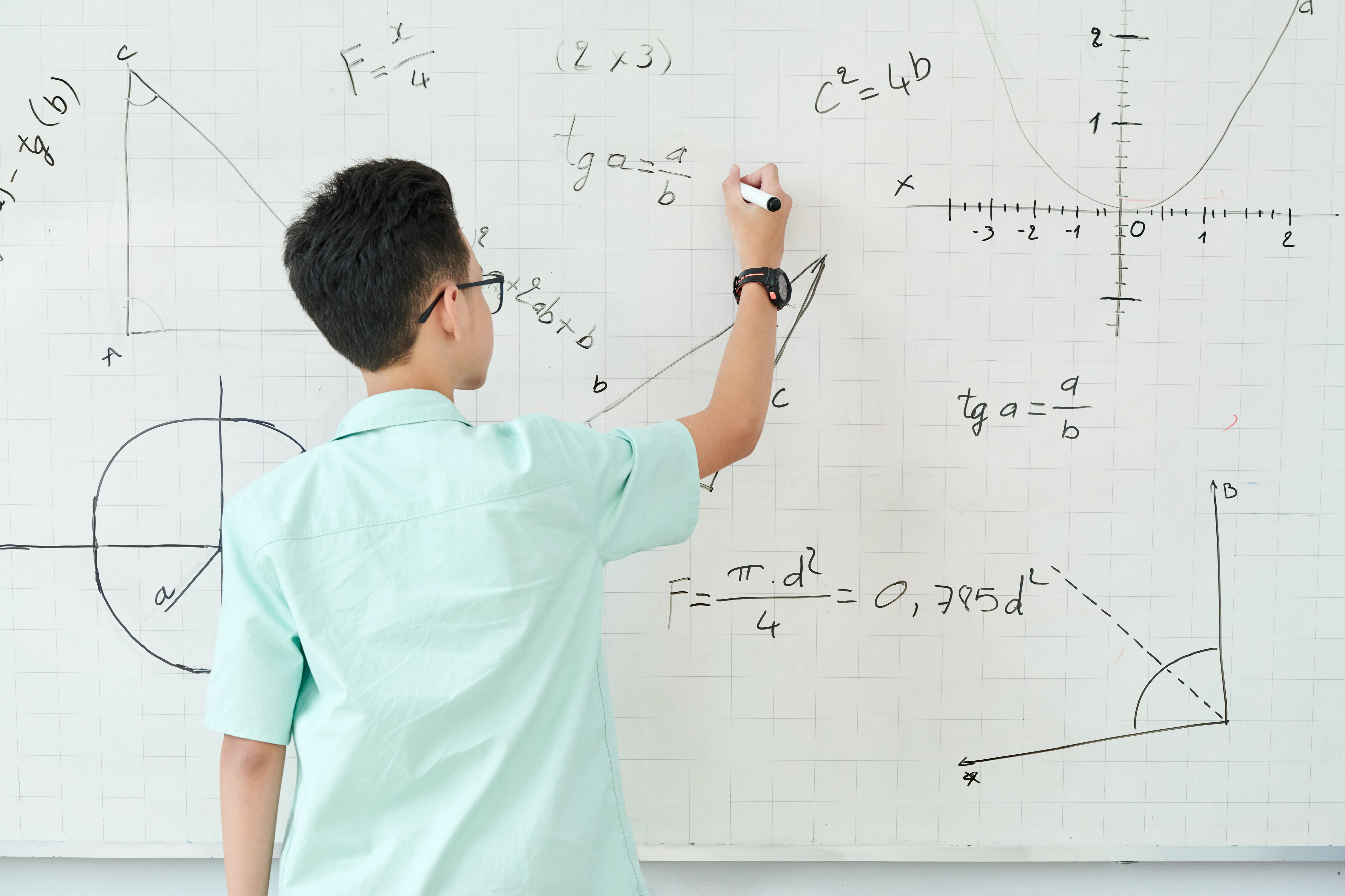 A person writing various mathematical equations and graphs on a whiteboard