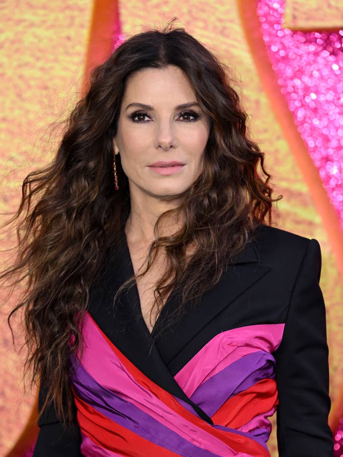 Sandra Bullock in an elegant black blazer with a striking purple and pink sash, posing at a formal event