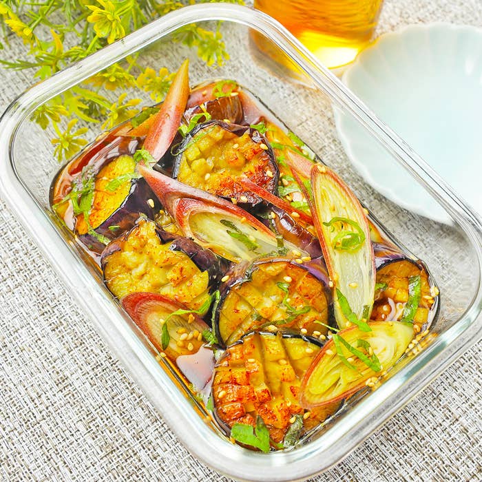 野菜のマリネ(なす、しょうが、ネギ)がガラス容器に入っている。背景には 飲み物が見える。